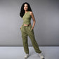 A woman with long dark hair models the Olive Corset Crop - Top with Parachute Pants, standing hands-in-pockets against a gray background.