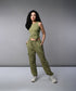 A woman with long dark hair models the Olive Corset Crop - Top with Parachute Pants, standing hands-in-pockets against a gray background.