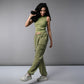 A woman smiles and walks against a plain gray background, wearing the Olive Corset Crop - Top with Parachute Pants, while holding a portable speaker.