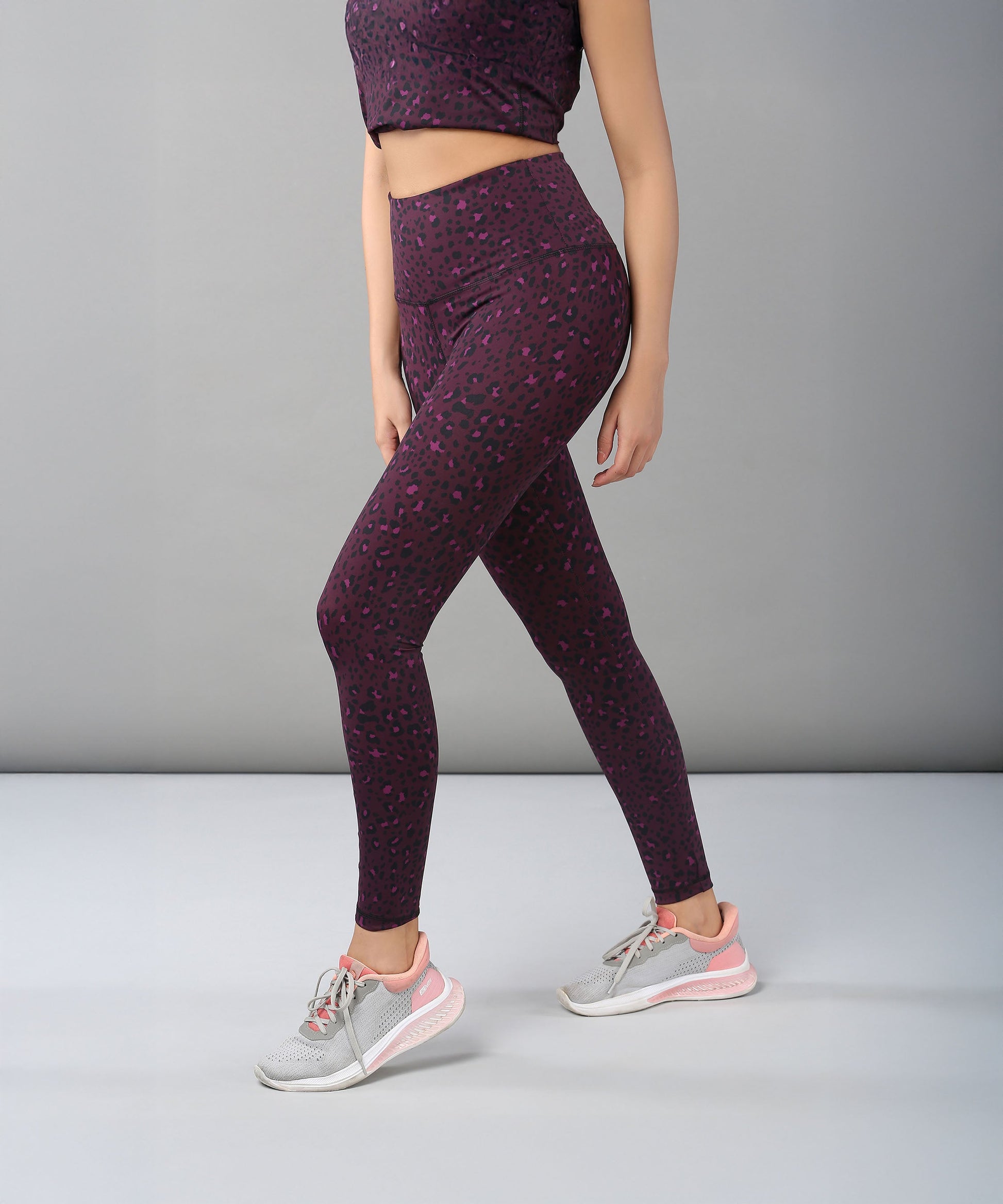 A woman wearing Pink Animal Print Leggings and gray sneakers stands against a plain gray background.