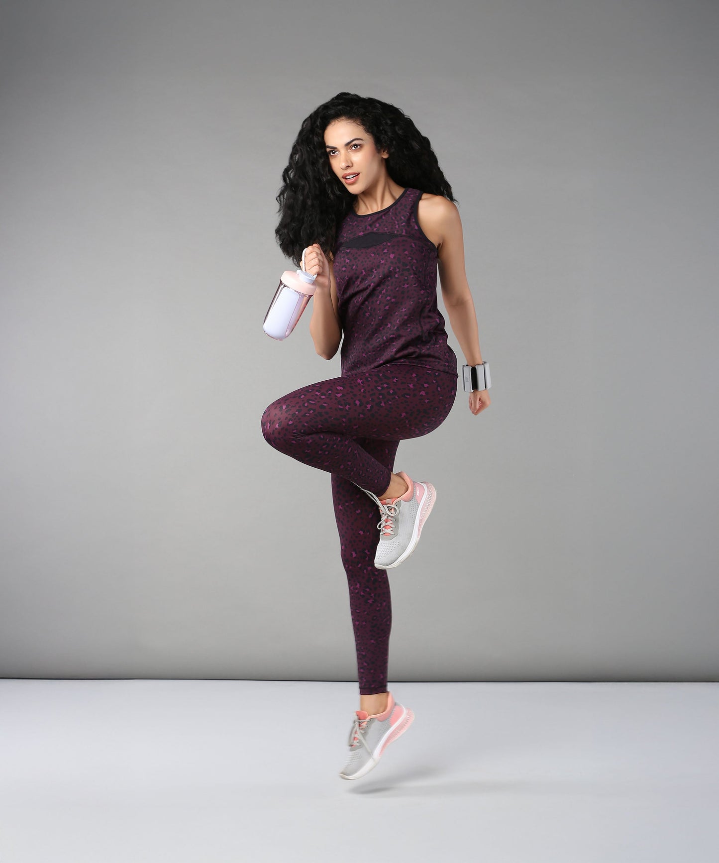 A woman wearing Pink Animal Print Leggings poses on one leg with a shaker bottle against a plain gray background.