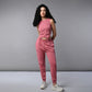 A woman with long curly hair wears a Pink Corset Crop-Top with Joggers and white sneakers, standing against a plain gray background.