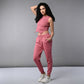 A woman confidently poses against a plain gray background wearing a Pink Corset Crop-Top with Joggers.