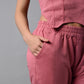A woman poses against a gray background wearing a Pink Corset Crop-Top with Joggers, crafted from cotton ribbed fabric, with one hand in her pocket.