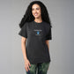 A smiling woman with long curly hair wears the Positive Body Image T Shirt in black, paired with tie-dye leggings.