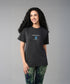A smiling woman with long curly hair wears the Positive Body Image T Shirt in black, paired with tie-dye leggings.