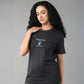 A woman with long curly hair stands against a gray background, wearing the Positive Body Image T Shirt, a black half-sleeve basic tee with "Positive Body Image" printed on it, highlighting her confident and empowering presence.