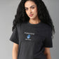A woman with long curly hair smiles against a gray background, wearing the Positive Body Image T Shirt—a black, basic half-sleeve tee with a "Positive Body Image" print.