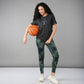 A smiling woman in a Positive Body image T Shirt and sporty outfit holds a basketball against a plain grey background, radiating confidence and positivity.