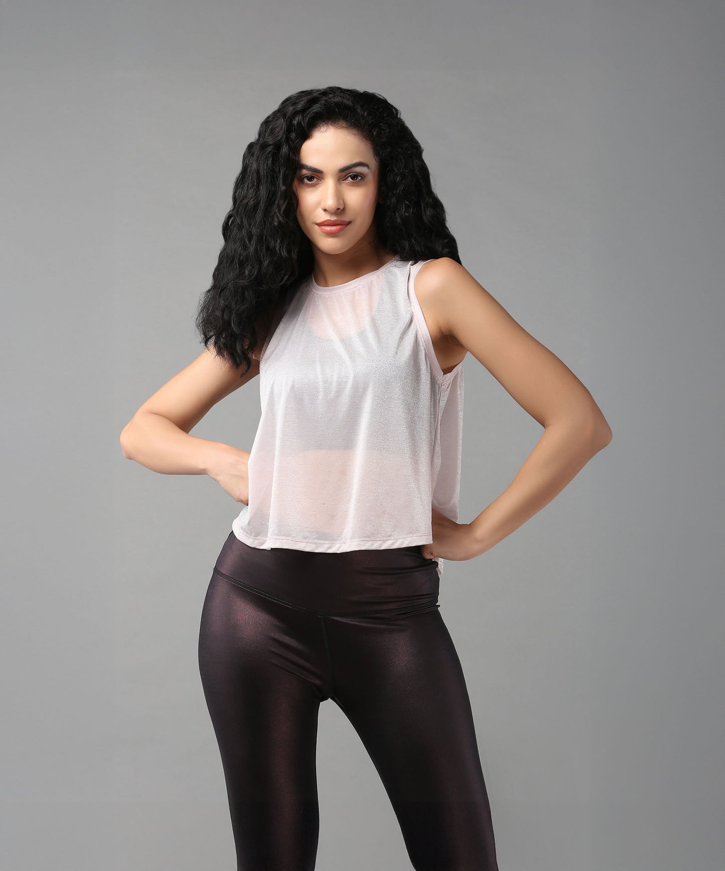 Woman with long curly hair poses confidently in a Powder Pink Sheer Top and black leggings.