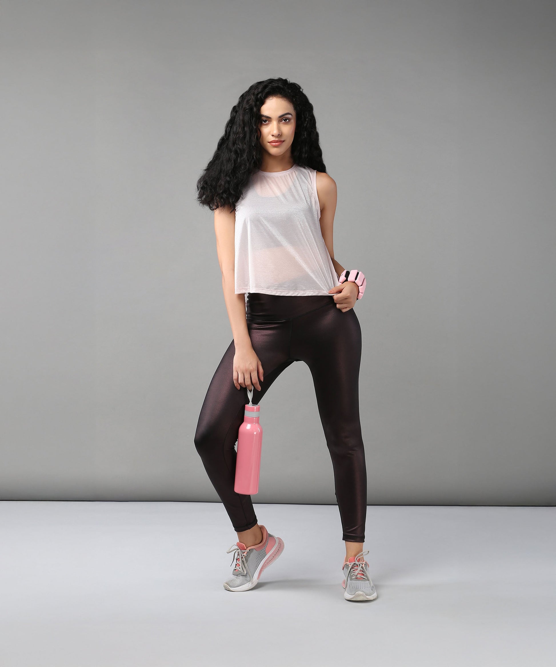Woman wearing the Powder Pink Sheer Top and workout clothes holds a pink water bottle, standing against a plain gray background.