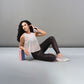 A woman in a Powder Pink Sheer Top and workout clothes sits on the floor, leaning against a yoga block and wearing wrist weights.
