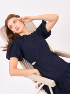 Female model wearing a navy blue dress from Stylera. styling over chair