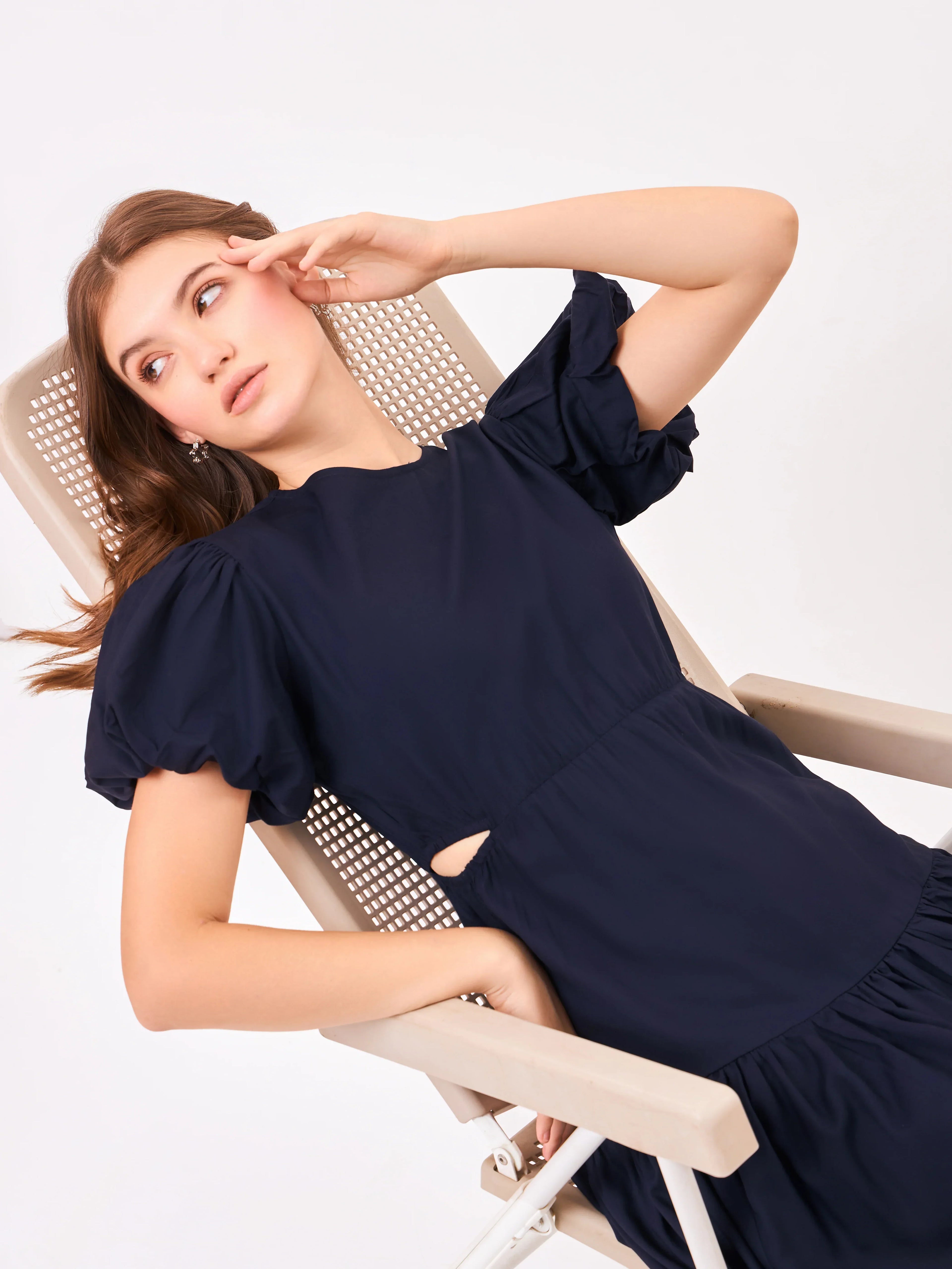 Female model wearing a navy blue dress from Stylera. styling over chair