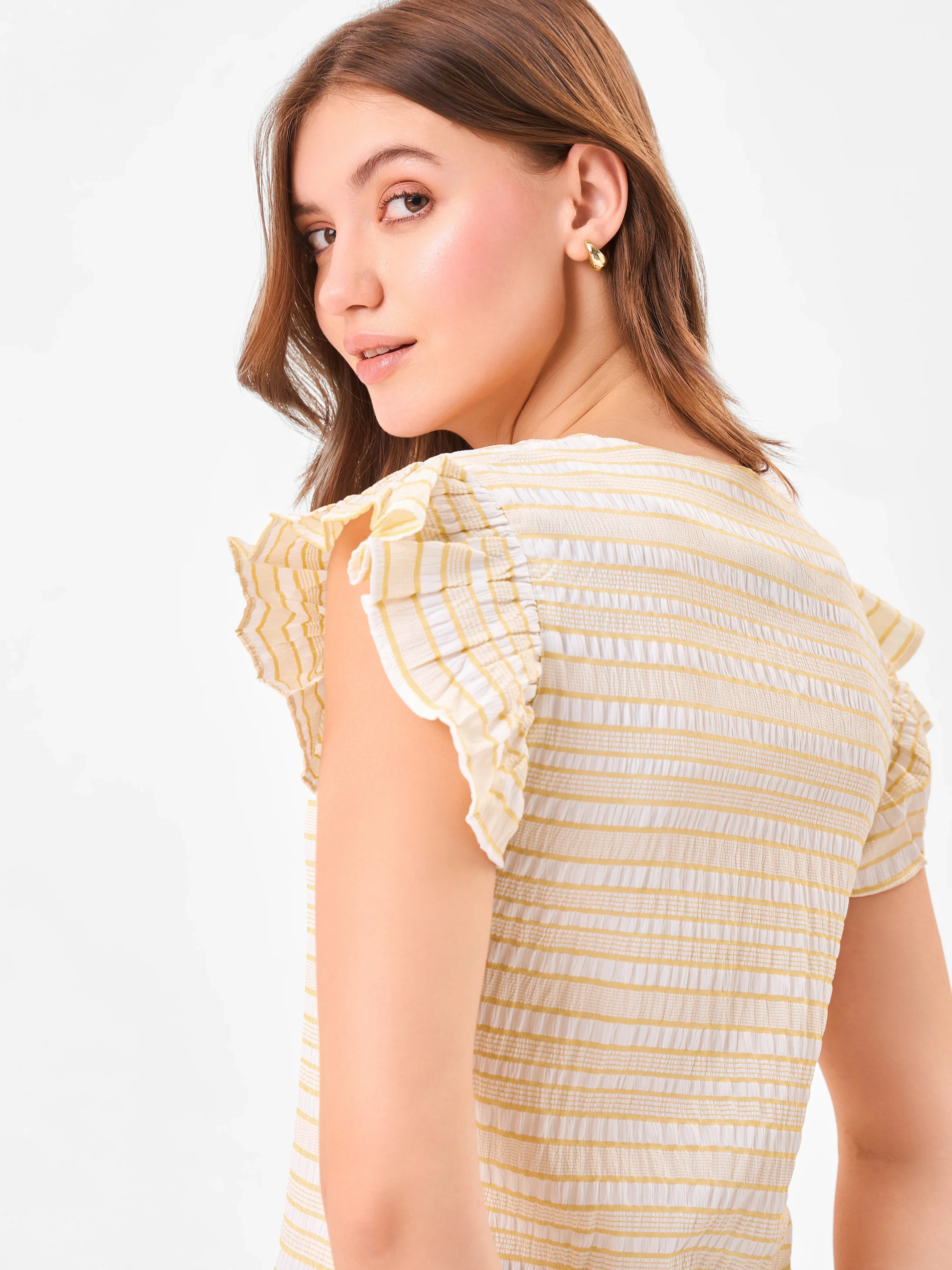 Female model wearing a yellow and white striped top with ruffled sleeves from Stylera, showcasing side