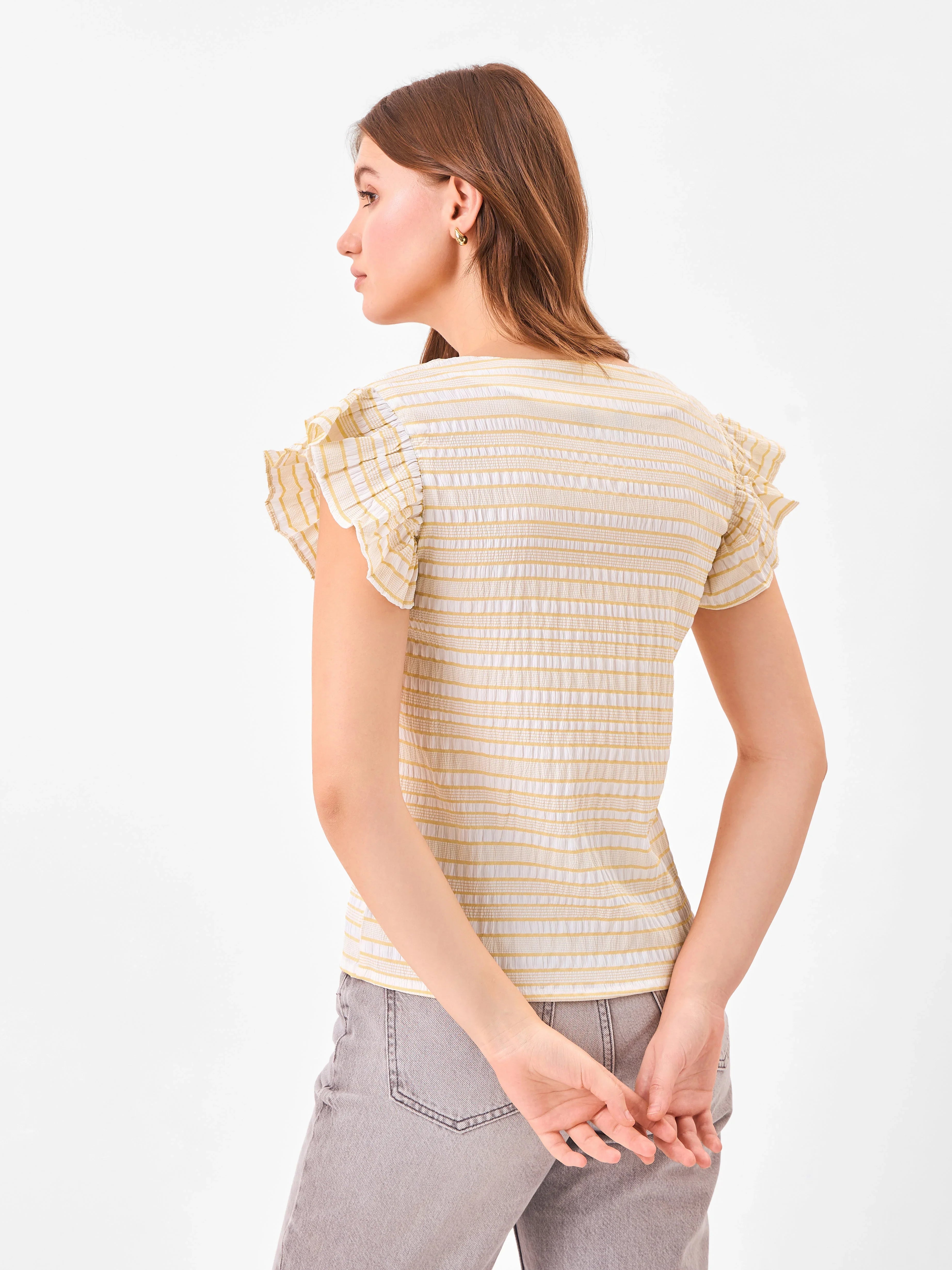 Female model wearing a yellow and white striped top with ruffled sleeves from Stylera, showcasing backside