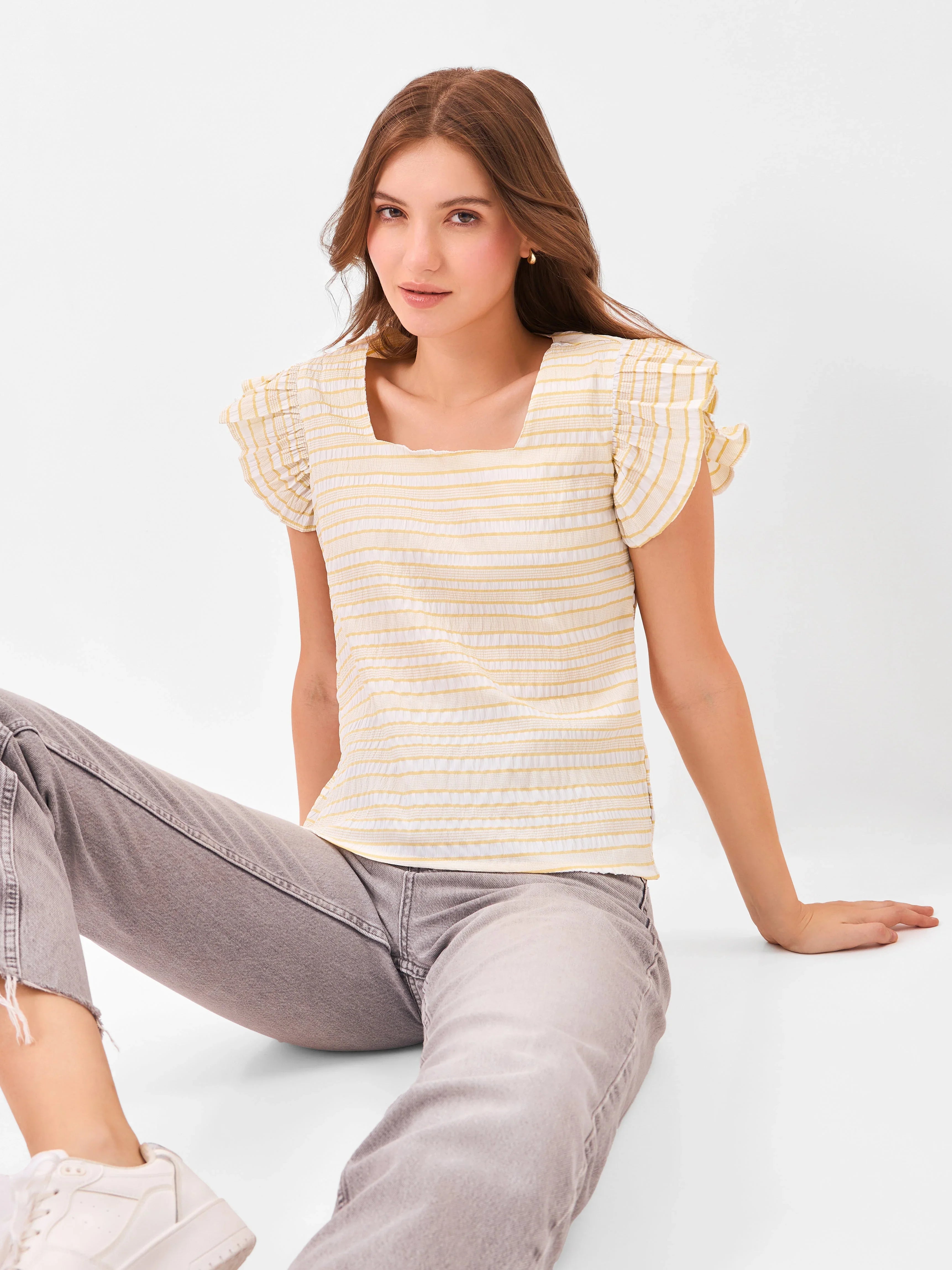Female model wearing a yellow and white striped top with ruffled sleeves from Stylera