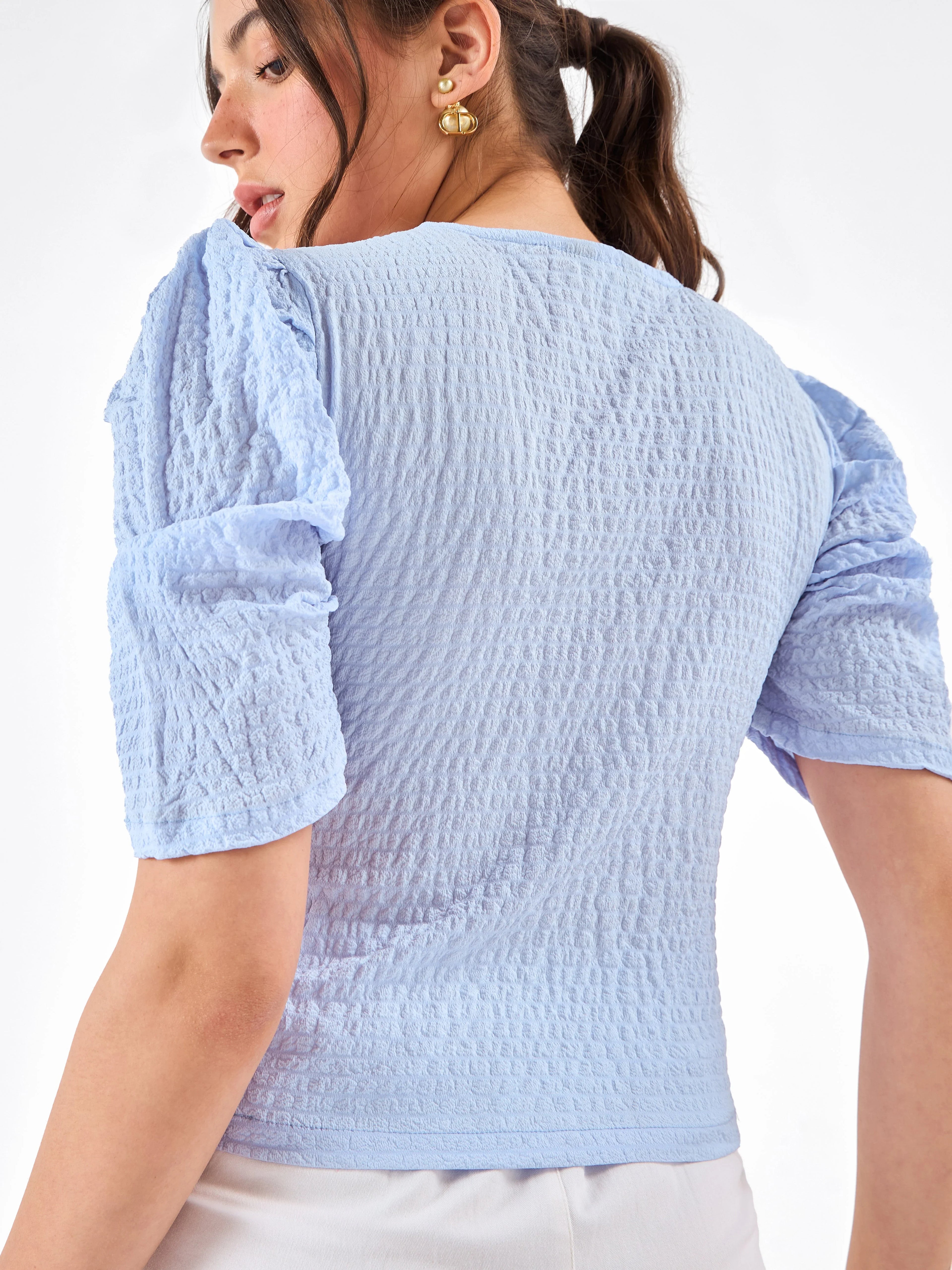 Female model wearing a light blue top from Stylera, showcasing backside