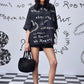 Stylera model wearing black scribble print shirt oversized hoodie style with shorts and black bag