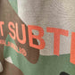 Stylera camo bowling shirt close up of green and brown camouflage fabric with coral graphic text