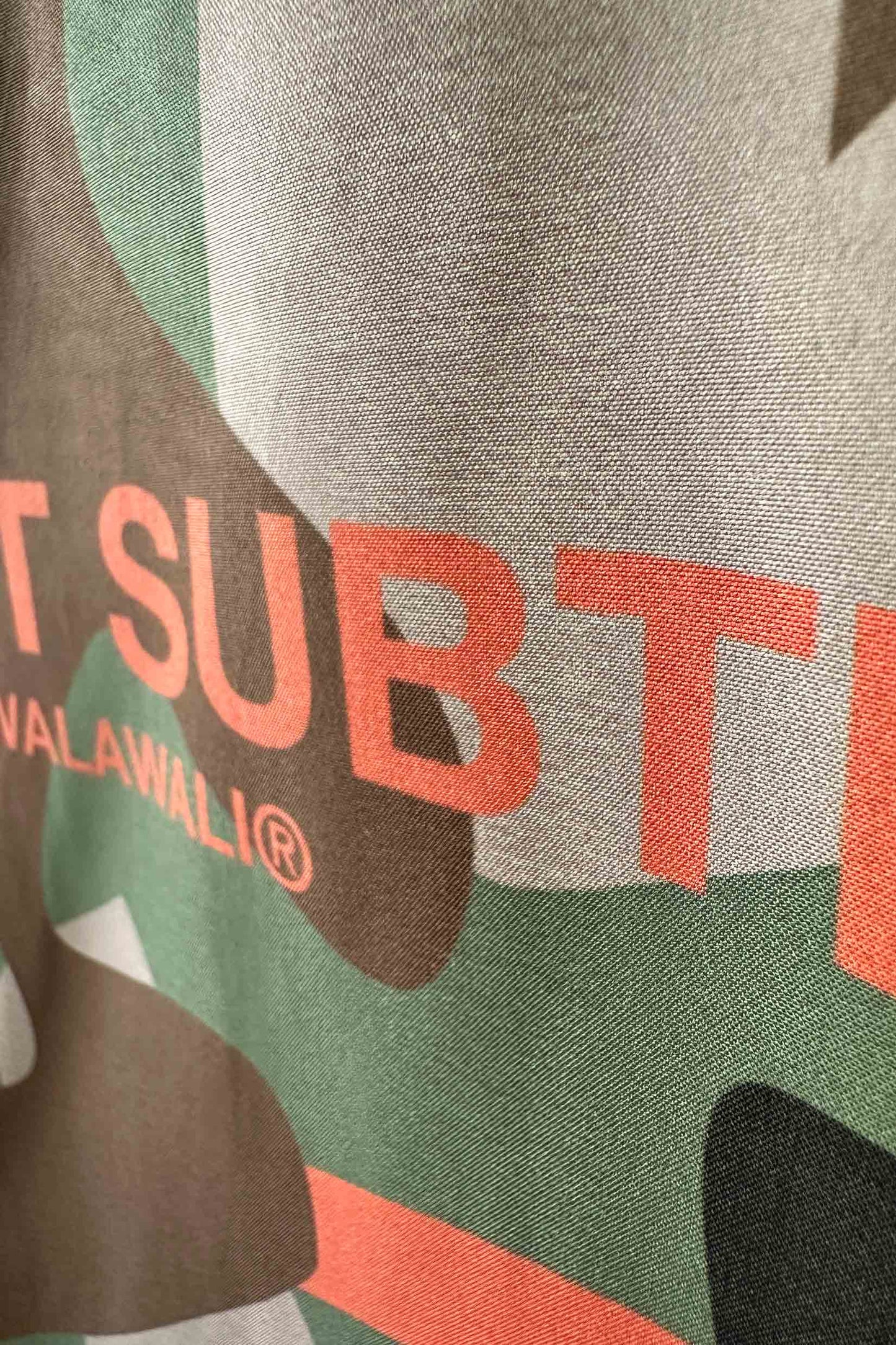 Stylera camo bowling shirt close up of green and brown camouflage fabric with coral graphic text