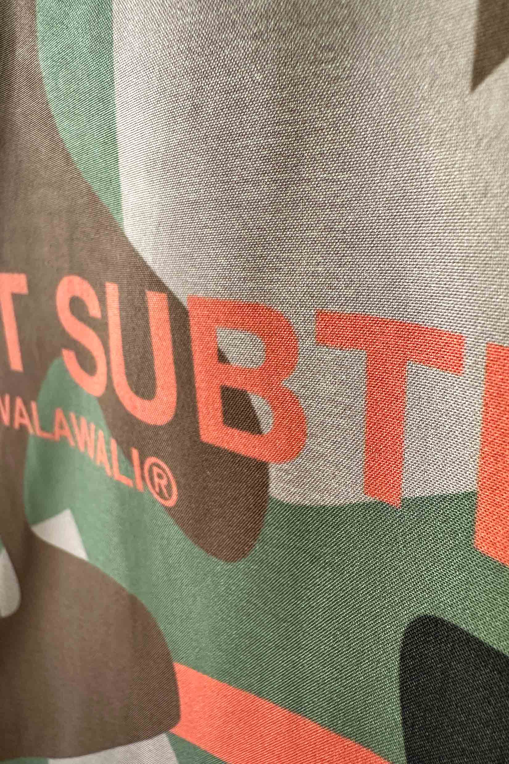 Stylera camo bowling shirt close up of green and brown camouflage fabric with coral graphic text
