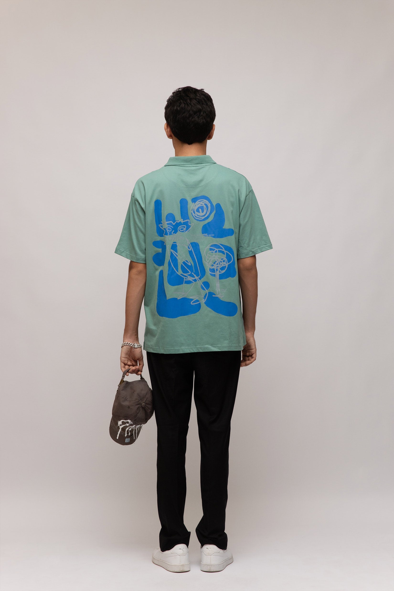 Stylera casual men's fashion polo mint green with blue back graphic worn by model holding cap and black pants