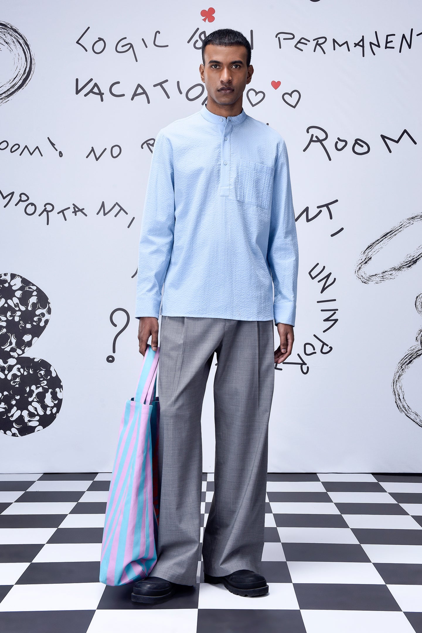 Man wearing a light blue regular fit shirt by Stylera paired with gray pants and holding a striped tote bag