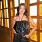 Model wearing Luna high waisted shorts in black sequins with satin bow halter top by wooden window