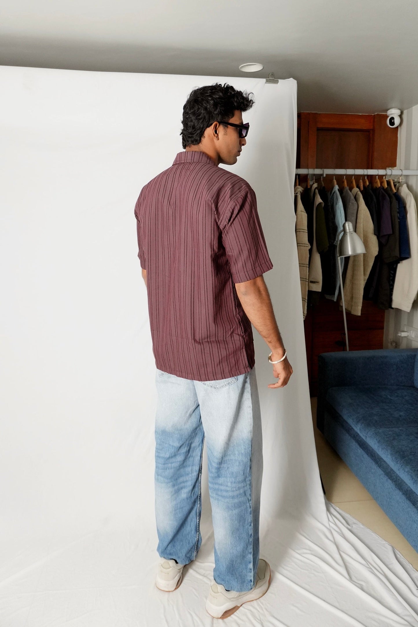 Rear view of model wearing Stylera men's maroon striped shirt with light wash jeans in studio