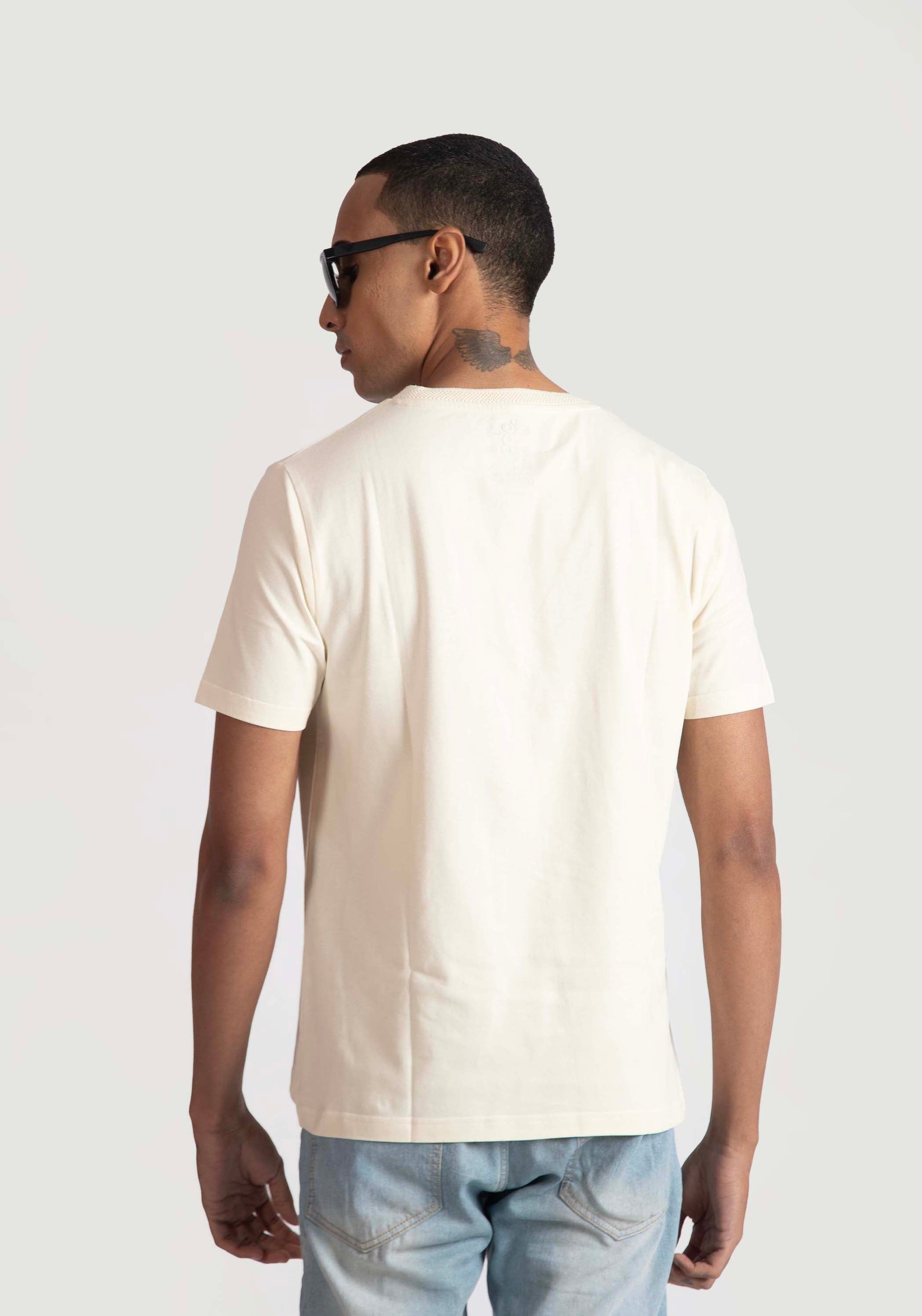 Back view of man wearing men's trendy cream t-shirt by Stylera paired with light blue jeans