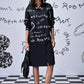 Model wearing Stylera oversized black shirt dress trendy with white script print long sleeves side slit and sneakers