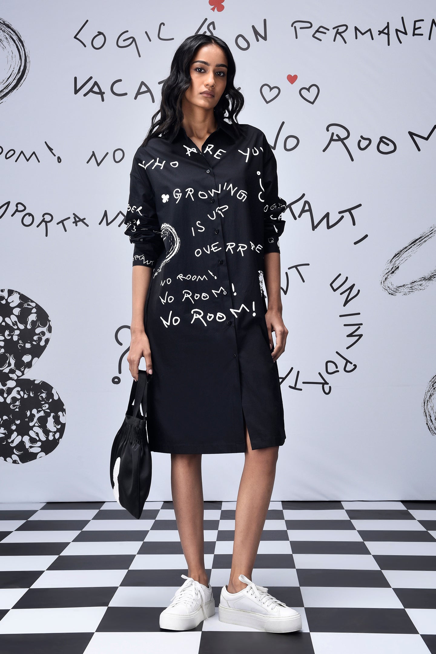 Model wearing Stylera oversized black shirt dress trendy with white script print long sleeves side slit and sneakers