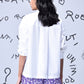 Back view of woman wearing white sequin heart shirt women by Stylera with purple floral shorts