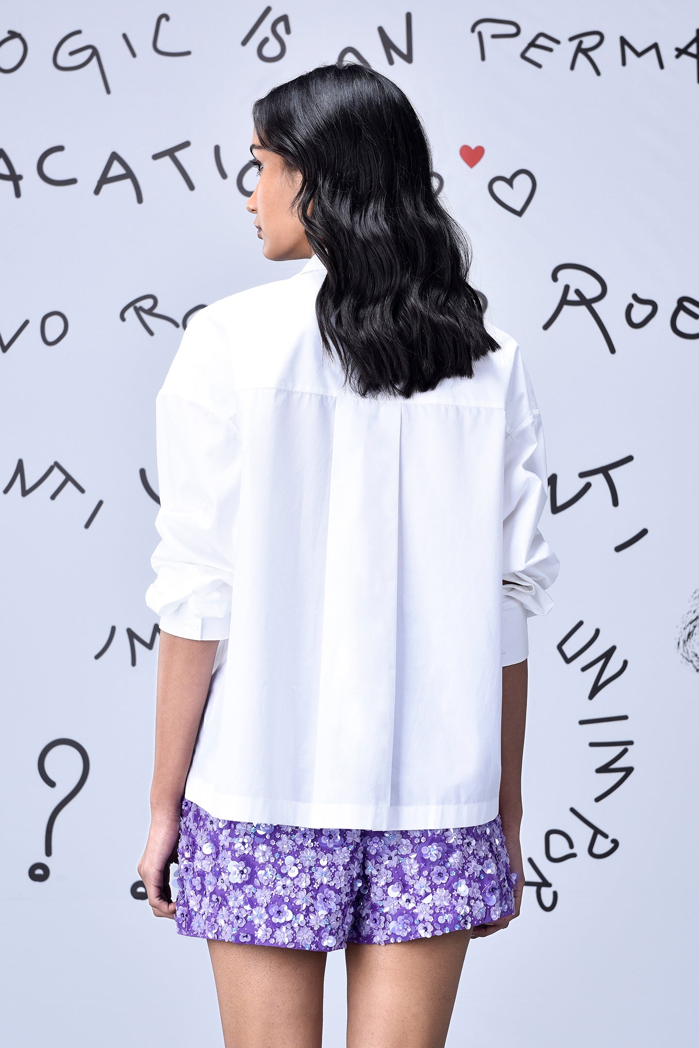 Back view of woman wearing white sequin heart shirt women by Stylera with purple floral shorts