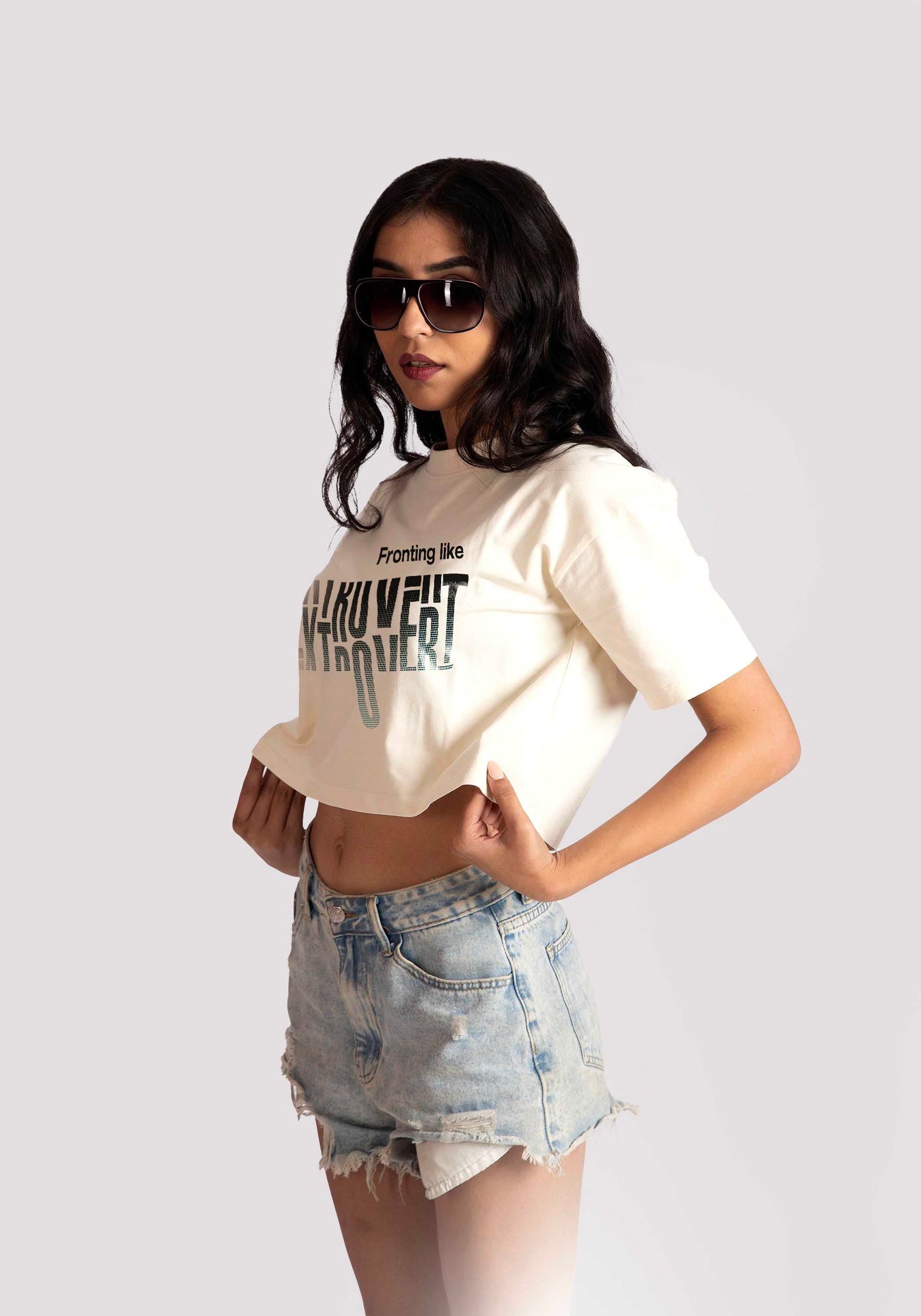 Woman wearing white oversized crop fit tee with graphic text and denim shorts by Stylera