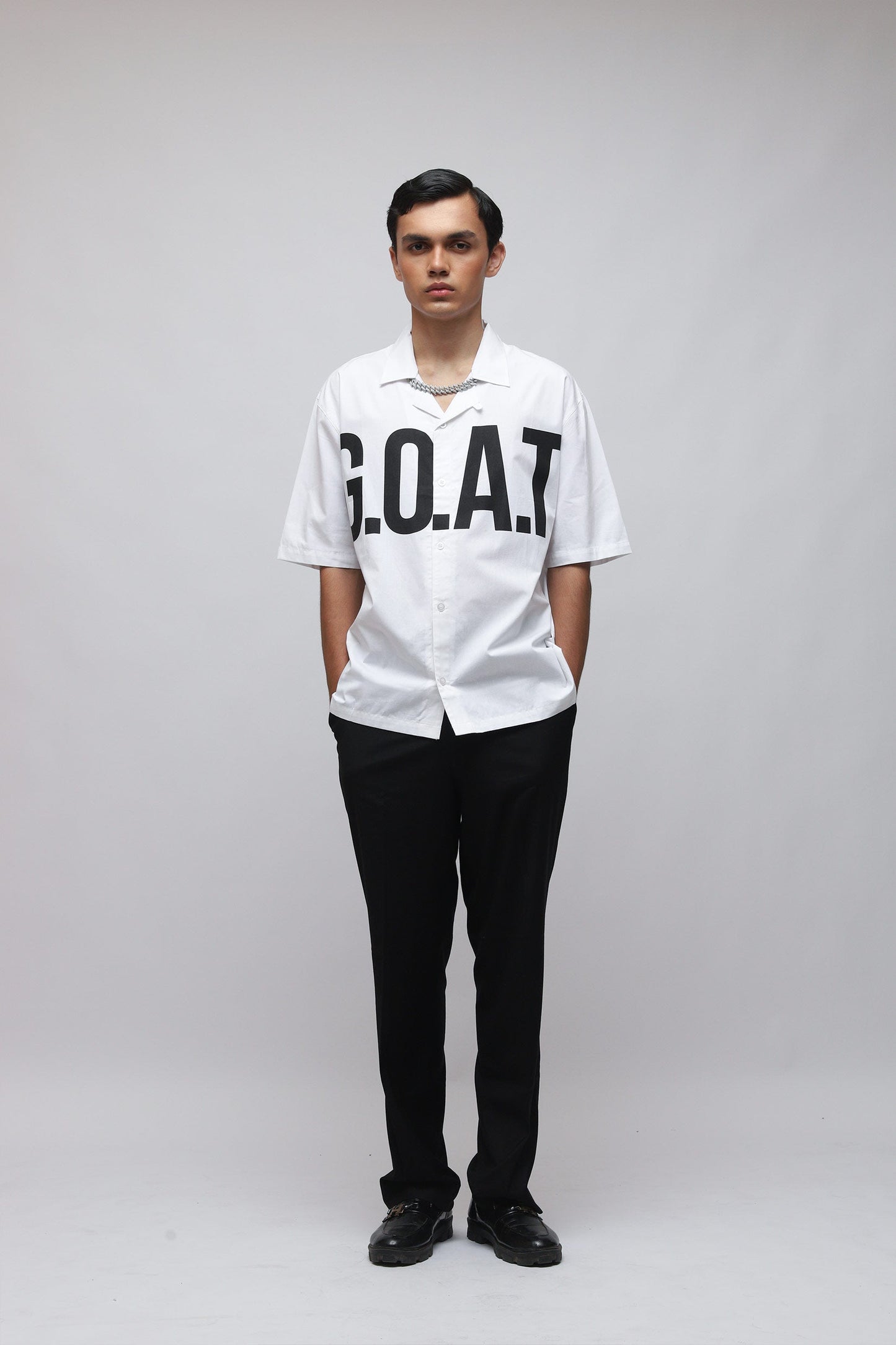 Stylera model wearing white trendy summer shirt with bold GOAT chest print short sleeves black pants