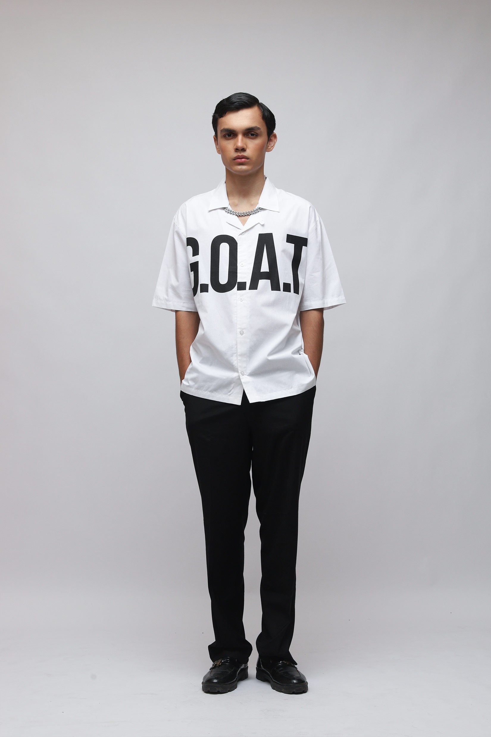 Stylera model wearing white trendy summer shirt with bold GOAT chest print short sleeves black pants
