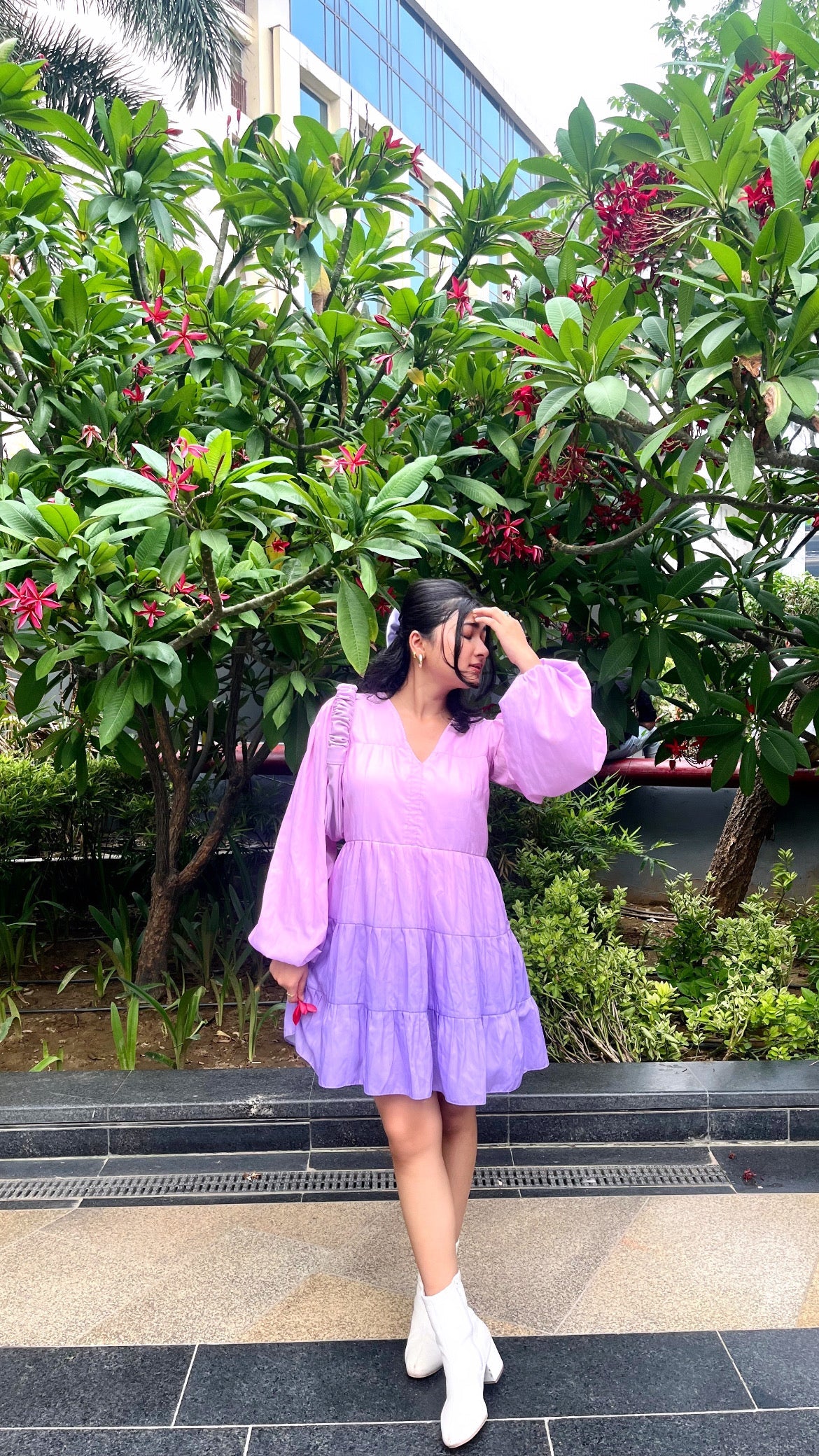 Model in women's purple gradient dress with puff sleeves and tiered skirt, white ankle boots, standing by tropical foliage