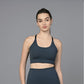 A woman wearing a Teal Sports Bra stands against a plain gray background, facing the camera.