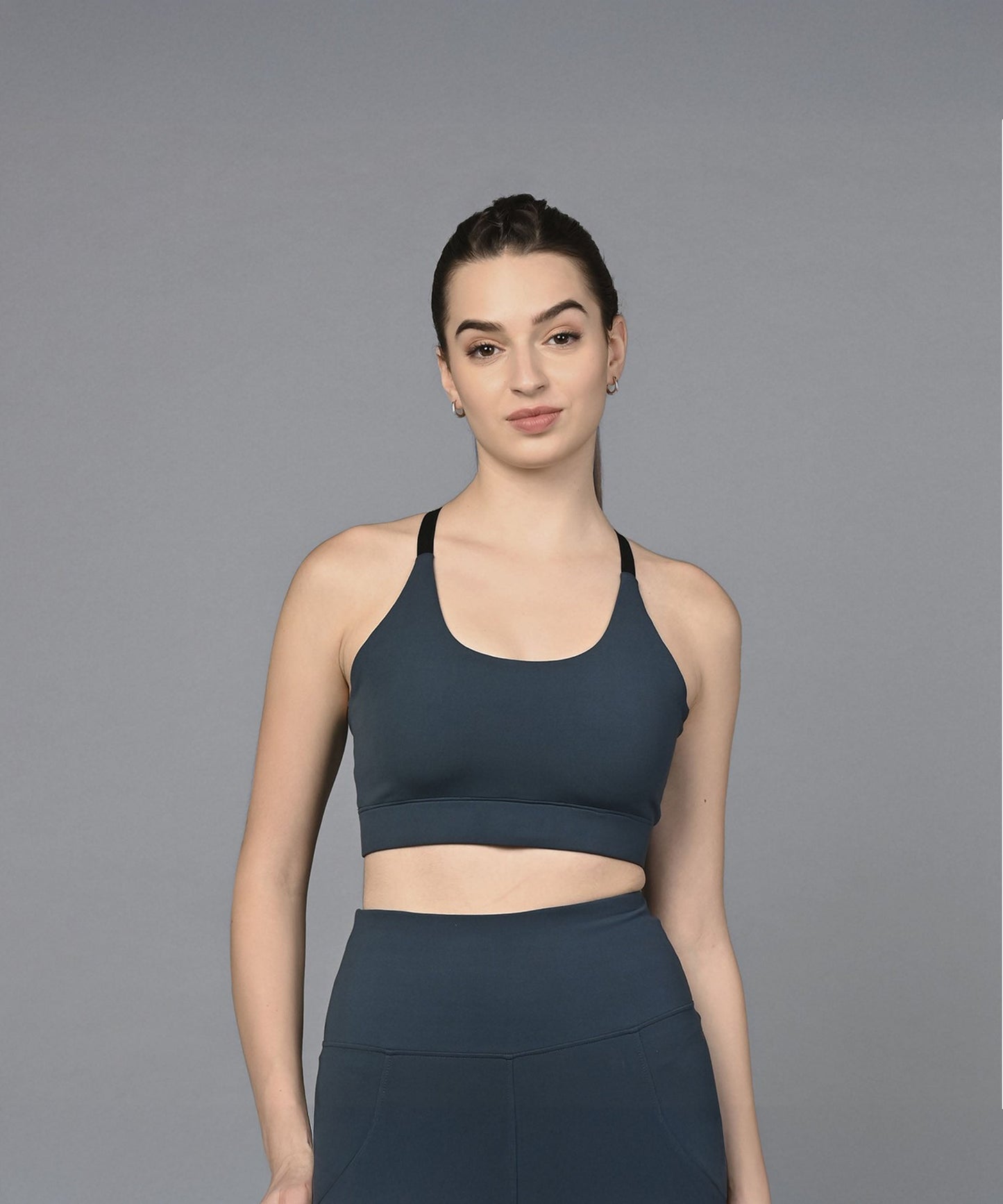 A woman wearing a Teal Sports Bra stands against a plain gray background, facing the camera.