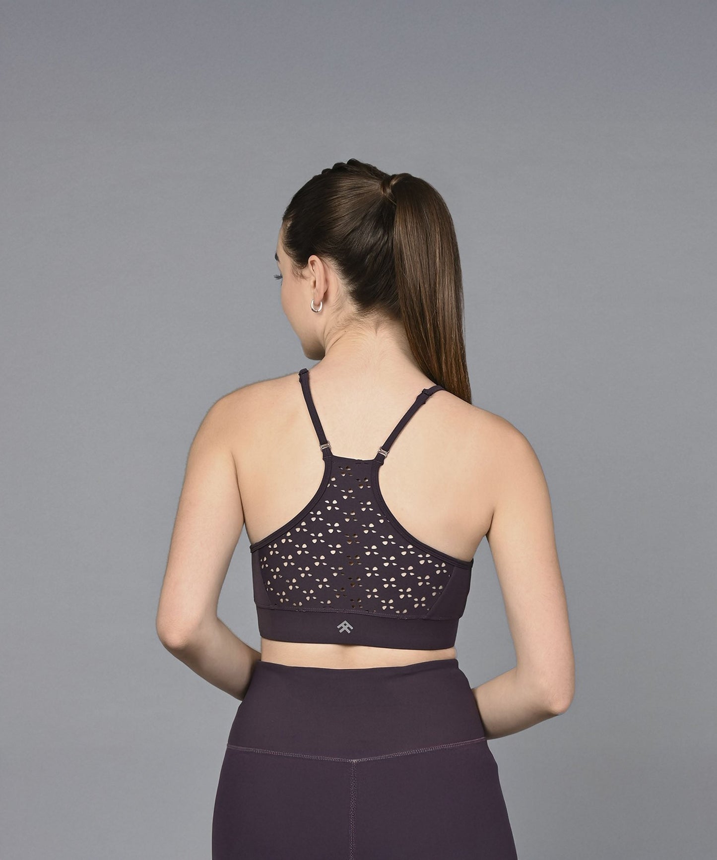 A woman with a ponytail is shown from the back against a gray background, wearing the Wine Sports Bra—a moisture-wicking fitness garment in dark wine.