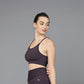 A woman in the Wine Sports Bra, featuring dark purple, moisture-wicking fabric, stands against a plain grey background and looks to the side.