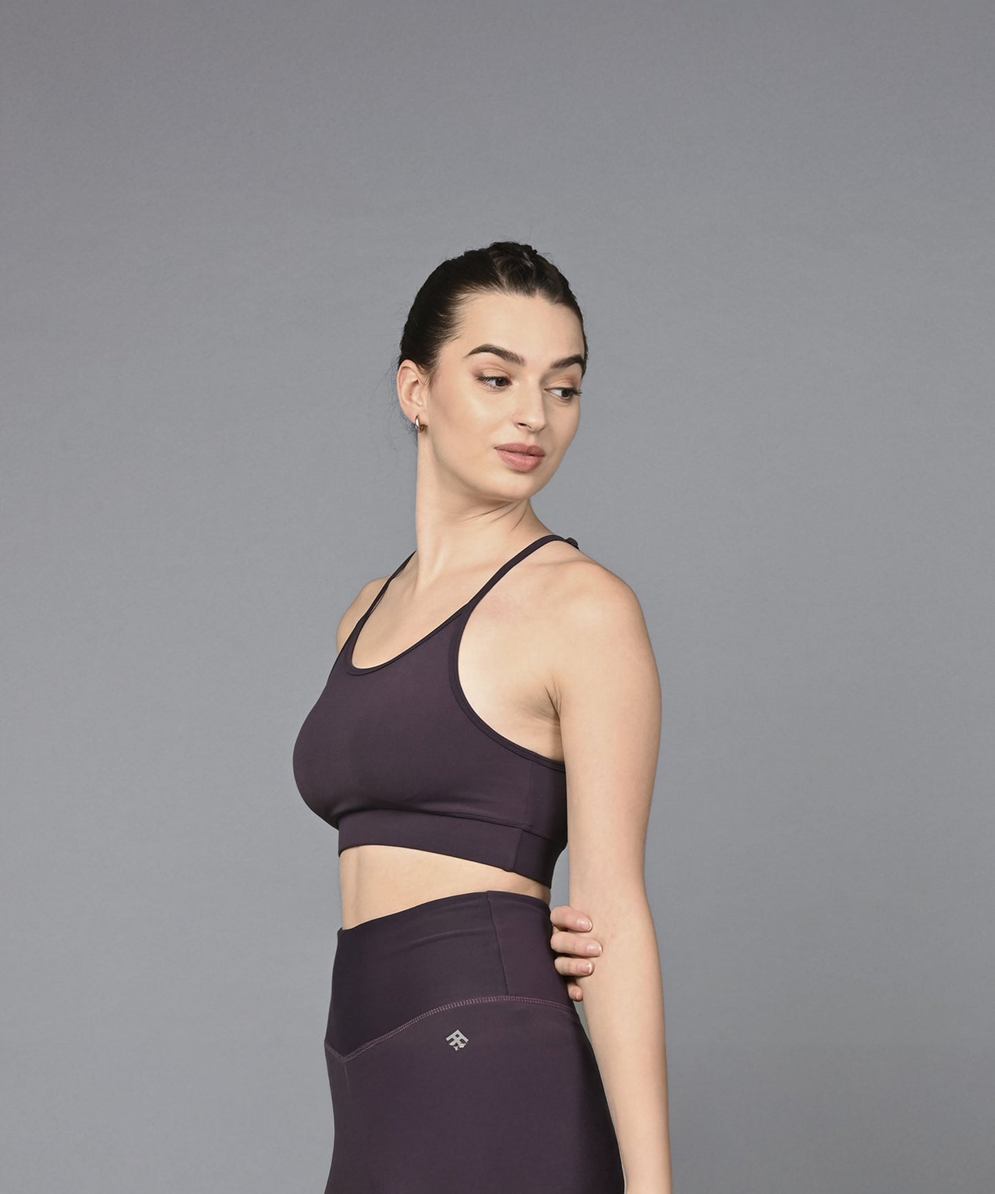 A woman in the Wine Sports Bra, featuring dark purple, moisture-wicking fabric, stands against a plain grey background and looks to the side.