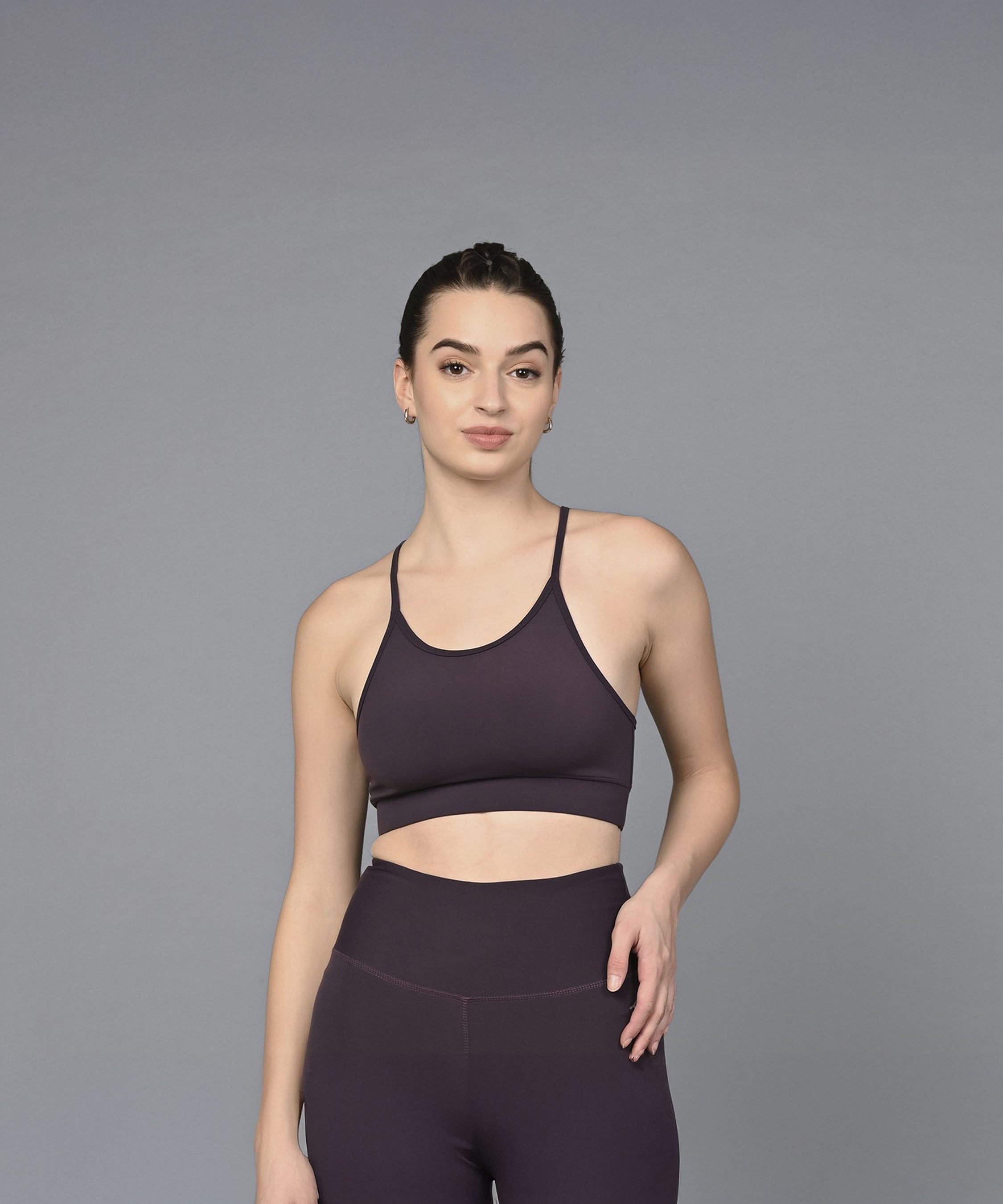 A woman models the Wine Sports Bra, paired with matching leggings, against a plain gray background.