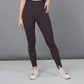 A woman models the Wine Leggings, featuring a dark botanical print and studded ankle details, paired with white sneakers against a gray background.