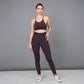 A woman in a dark purple sports bra and Wine Leggings stands against a plain gray background.
