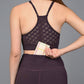 A woman in workout clothes, wearing the Wine Sports Bra, slips a cardholder into the back pocket of her leggings.