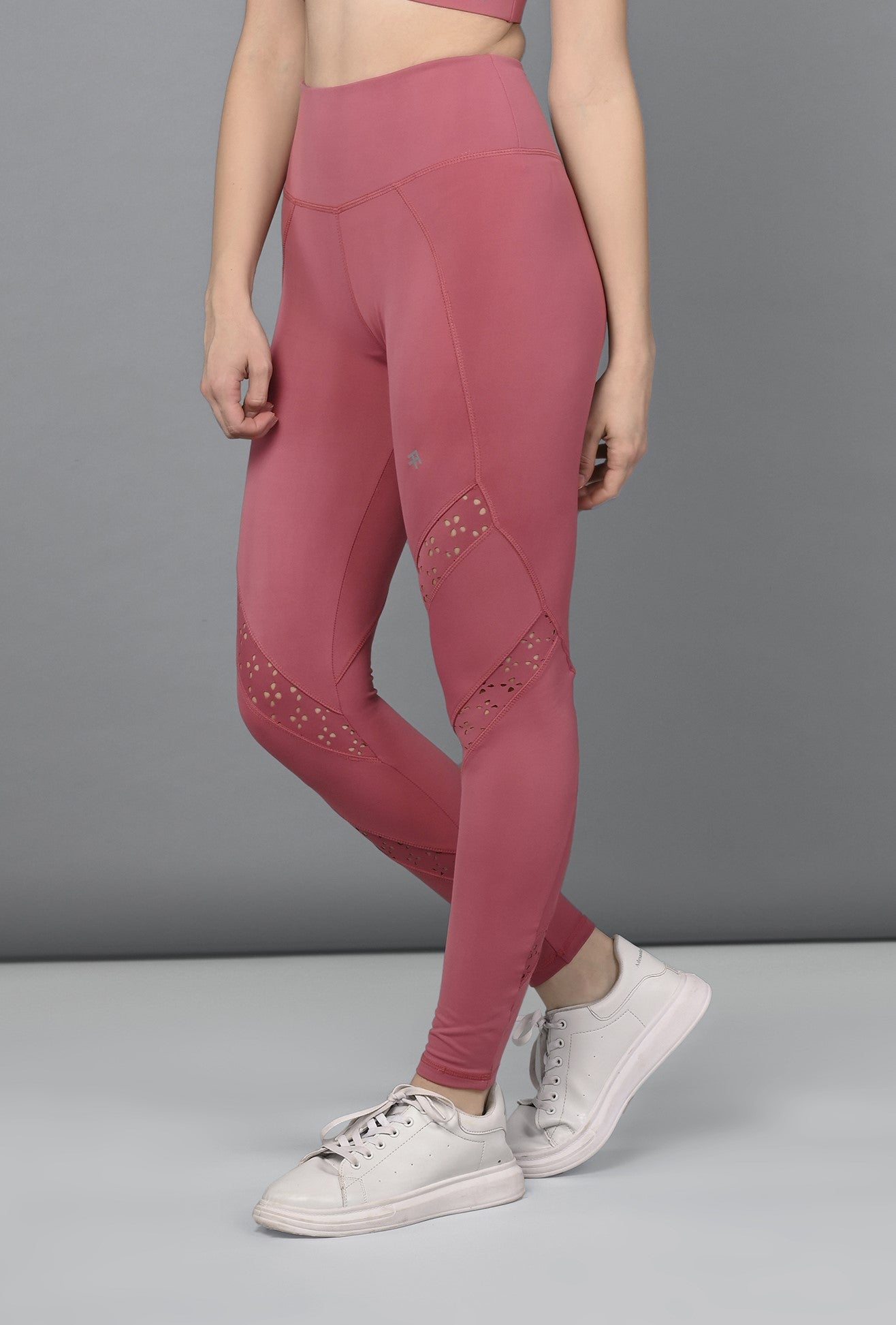 A woman stands against a gray background wearing Peony Pink Leggings with mesh panels and white sneakers.