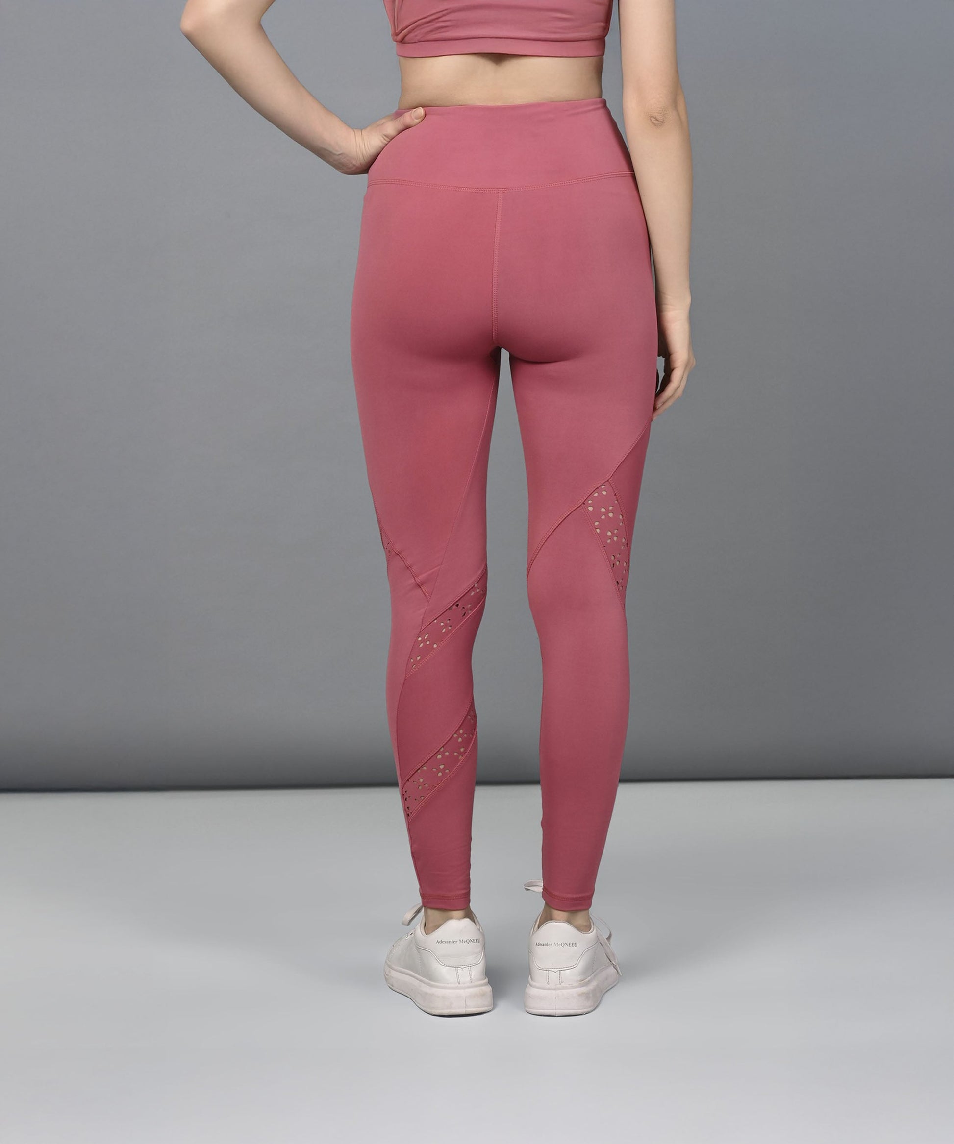 A woman shows off Peony Pink Leggings, paired with white sneakers, standing with her back to the camera against a plain grey background.